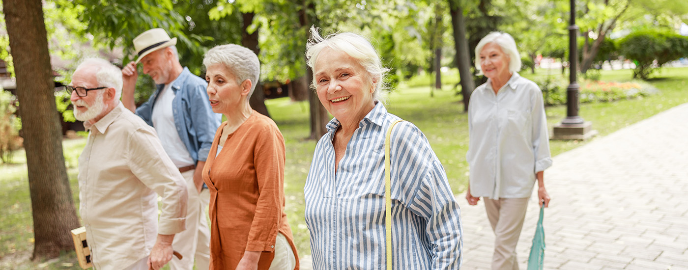 Group of two male and three female seniors walk on a paved path outdoors while one women smiles at the camera