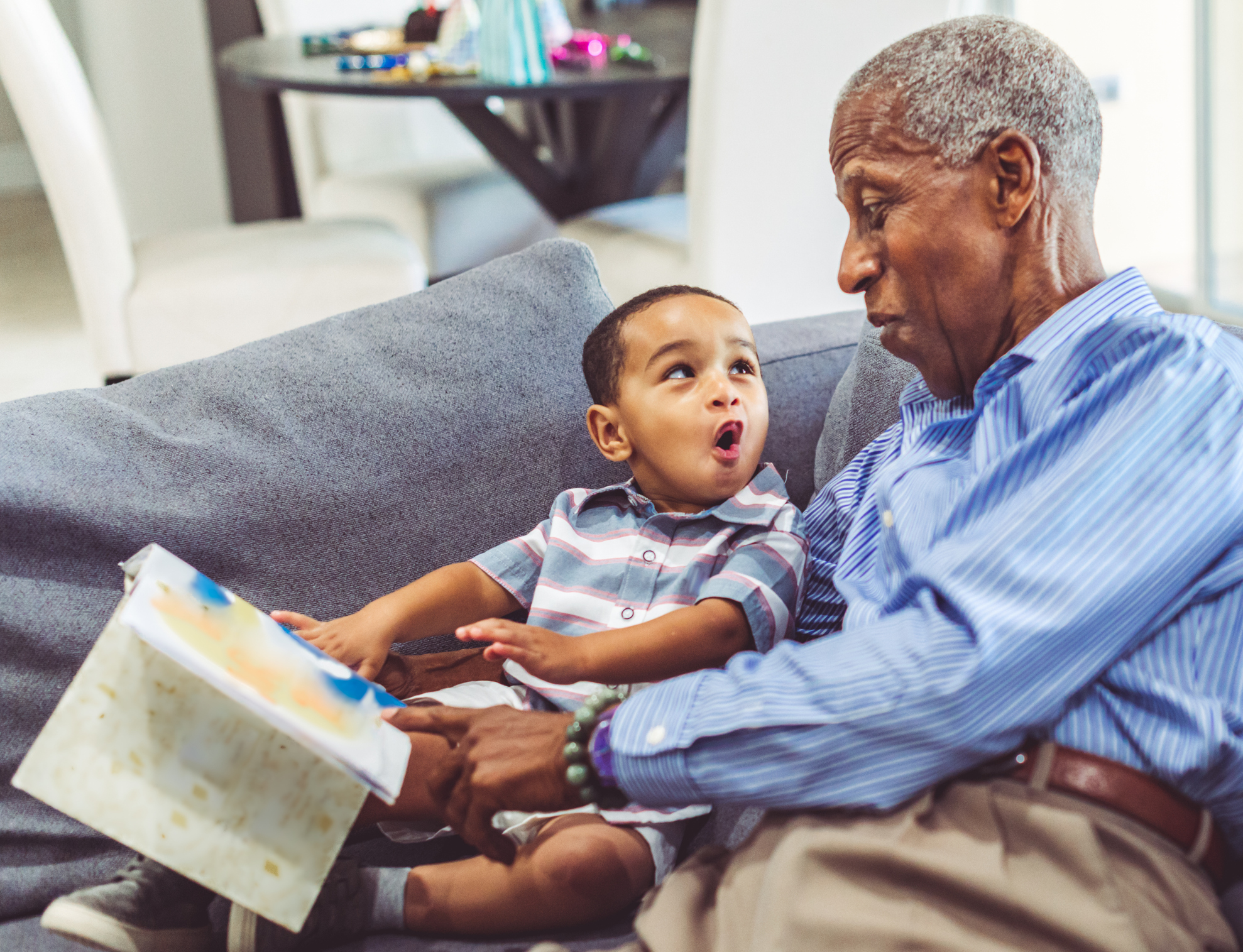 African American grandchild and grandfather read a book together at home Adorable toddler with his grandfather relaxing at home reading a book together