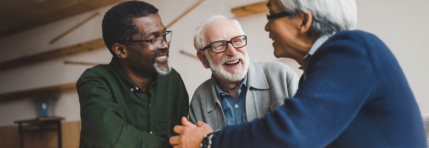Group of three senior men sit together at a table and laugh